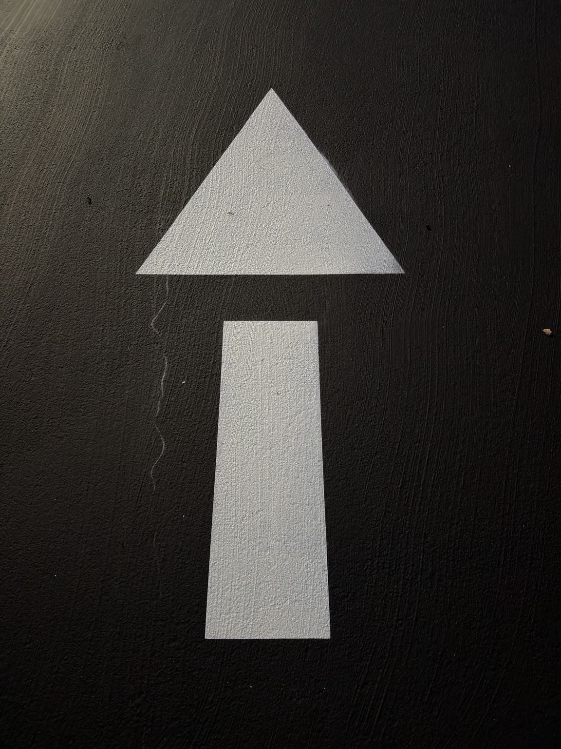 Complete freshly painted white directional arrow on dark asphalt